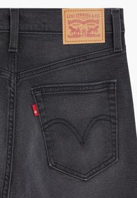 Black denim jeans featuring a rear pocket with a classic curved seam and a small red tab, topped with a brown leather brand patch.