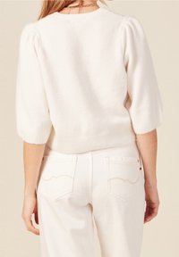 Maglione bianco e soffice a maglia con maniche a palloncino corte, orlo a coste e scollatura ampia, abbinato a jeans chiari a vita alta.