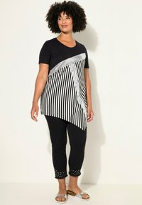 Top a righe bianche e nere con un'accento argentato, abbinato a pantaloni cropped neri con orli borchiati e sandali bassi.
