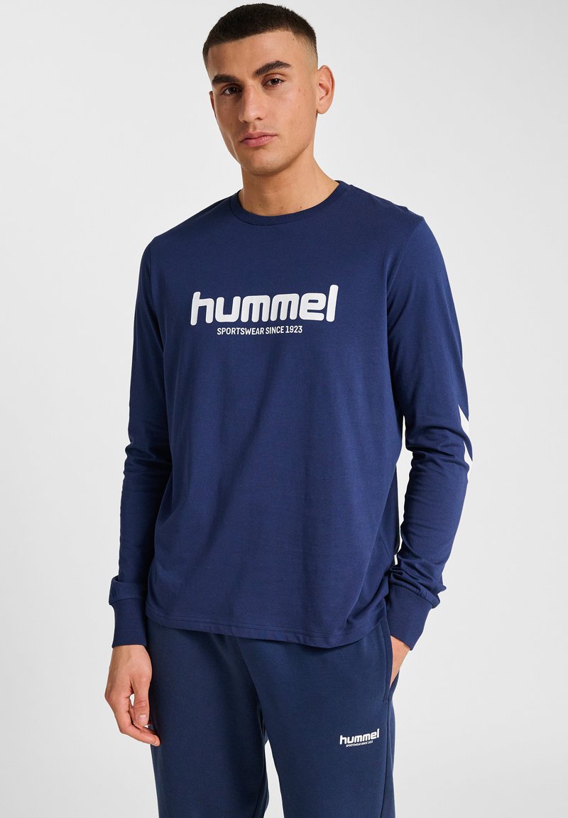 Mörkblå långärmad skjorta gjord av mjukt tyg, med en stor vit "hummel"-logotyp på bröstet och vita accenter på ärmarna.