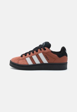 Baskets Adidas Campus à profil bas en brun rouille avec semelle noire, lacets noirs, bandes blanches caractéristiques et accents noirs au talon et à la languette.