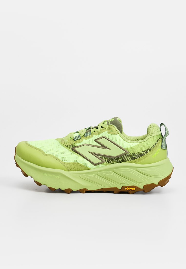 Zapatilla deportiva verde claro con suela gruesa, parte superior de malla, logo de New Balance y suela Vibram, vista desde el lateral sobre un fondo liso.