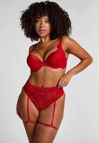 Conjunto de lencería de encaje rojo que incluye un sujetador estructurado con tirantes decorativos y un cinturón liga de talle alto a juego con paneles transparentes y detalles.