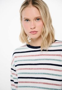 Gestreepte trui van zachte gebreide stof met horizontale strepen in marineblauw, roze en groen op een witte achtergrond, met een ronde hals.