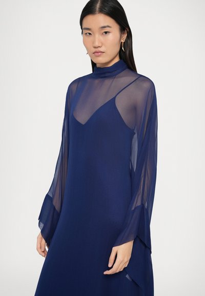 Rochie albastru închis cu mâneci lungi din material transparent și guler înalt. Prezintă un strat interior mulat și un strat exterior fluid pentru un aspect stratificat.