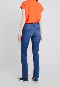 Tmavě modré džíny s rovný fit, které mají dvě zadní kapsy a jemné detaily šití, ve spojení s jasně oranžovým topem.