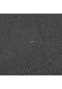 Gray knitted sweater with a ribbed hem and a small metallic brand tag. Fabric shows a smooth texture with slight flecks.