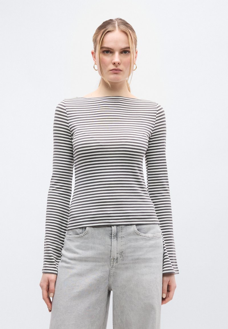 Ριγέ μπλούζα με μακριά μανίκια σε γκρι και λευκό βαμβάκι, με λαιμόκοψη καραβόπανο και στενή γραμμή. Φορεμένη με τζιν σε ανοιχτό γκρι.