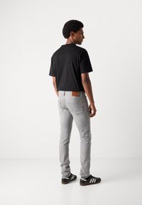 Zwarte polo met korte mouwen, grijze slim-fit jeans met een leren label en zwarte sneakers met witte strepen, gezien vanaf de achterkant.