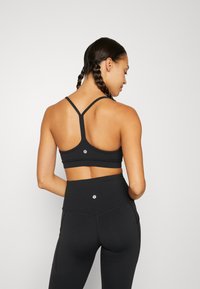 Zwarte sportbh met een racerbackontwerp en logodetail, gecombineerd met hoge zwarte leggings met een gladde textuur en naadaccenten.