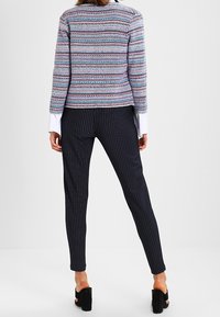 Pruhovaný pletený svetr v modré, růžové a bílé barvě, spárovaný s úzkými černými kalhotami s proužky. K outfitu dokonale ladí černé sandály na čtvercovém podpatku.