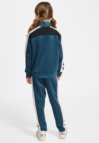 Trainingspak met een teal kleurige jas met zwarte accenten en witte zijstrepen, gecombineerd met bijpassende teal broeken, gemaakt van een soepele stof.