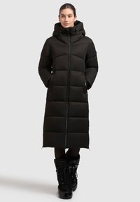 Musta pitkä toppatakki hupulla, jossa on edessä vetoketju, sivutaskut ja tikattu kuosi eristyksen ja lämmön takaamiseksi.