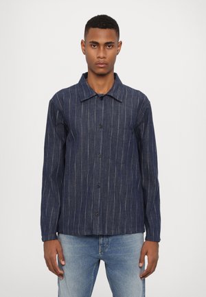 Camisa de denim azul marino con rayas blancas verticales, cierre de botones y un bolsillo en el pecho. Mangas largas y un diseño de cuello clásico.