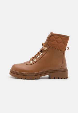 Bottine marron en matériau synthétique, avec un dessus matelassé, un bout rond, des œillets dorés et une semelle texturée.