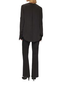 Zwarte zijden blouse met een ronde halslijn, lange mouwen en een plooitje aan de achterkant, gecombineerd met zwarte flared trousers en hoge hakken.