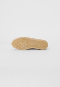 Suola di scarpa in gomma con intricato motivo a zigzag, color beige, dettaglio del logo circolare e bordo leggermente curvato per una migliore aderenza.