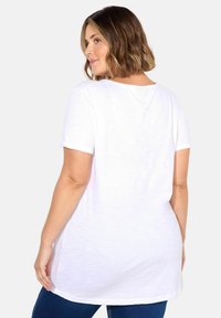 Valkoinen lyhythihainen t-paita, joka on valmistettu kevyestä kankaasta, rentoa istuvuutta ja pyöreää kaula-aukkoa, yhdistettynä sinisiin farkkuihin.