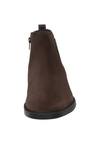 Braune Wildleder-Ankle Boots mit einer schwarzen Gummisohle, ausgestattet mit einem seitlichen Reißverschluss und einer roten sowie marineblauen Schlaufe an der Rückseite für einfaches An- und Ausziehen.