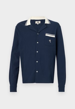 Marineblå skjorte med knapper lavet af et tekstureret stof, en hvid krave og en lomme med et hjerte design og stribede detaljer.