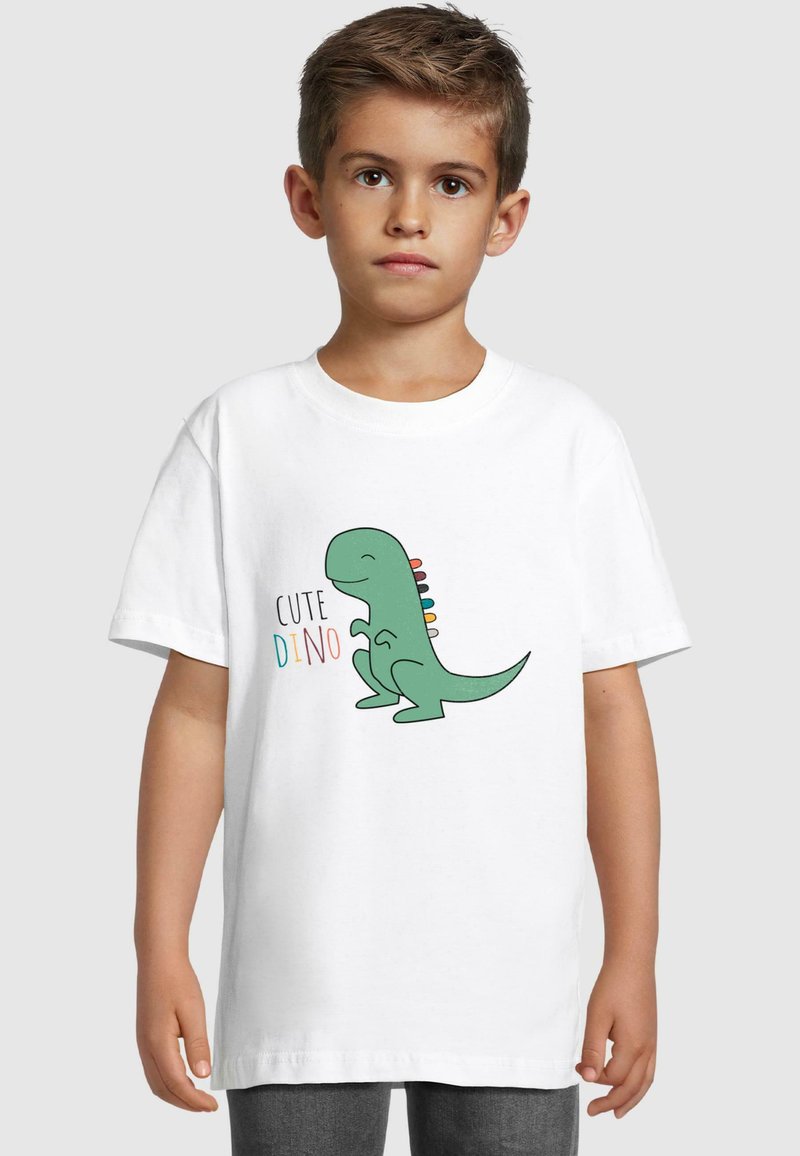 Balts kokvilnas T-krekls ar rotaļīgu zaļu dinozauru grafiku, kas rotāts ar daudzkrāsainiem ērkšķiem un uzrakstu "CUTE DINO" dažādās krāsās.