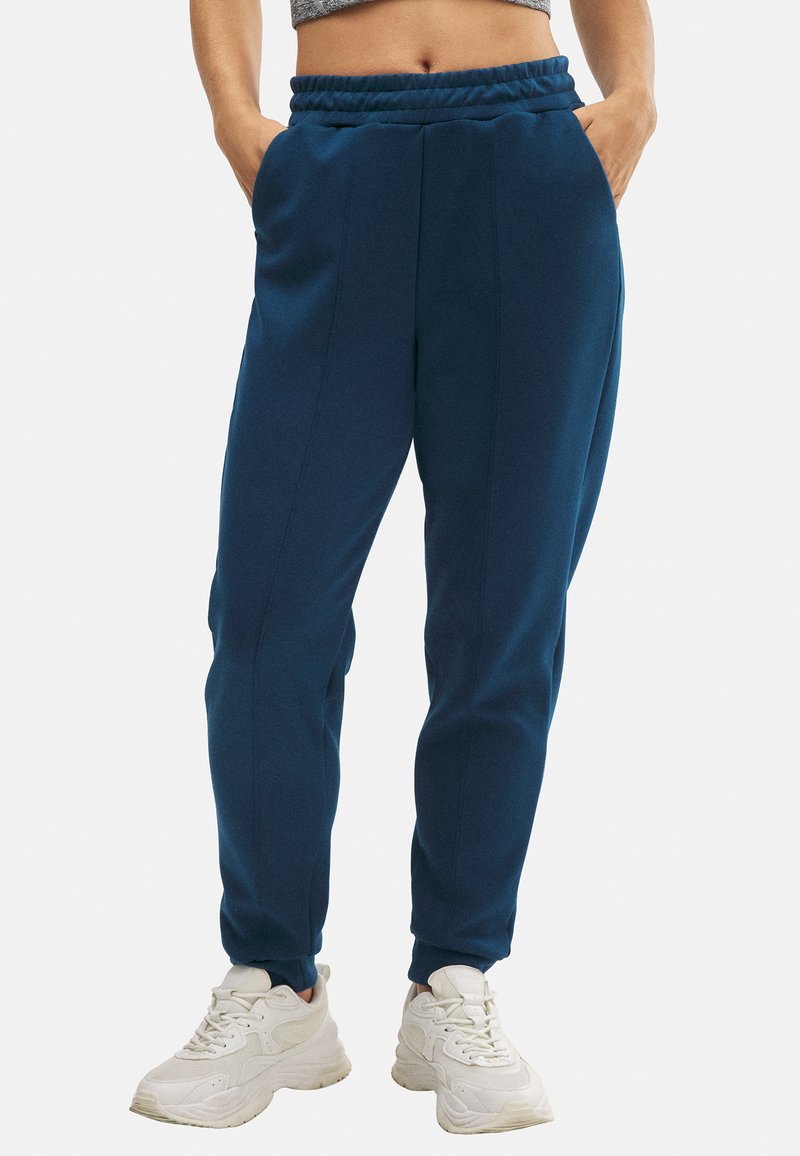 Pantalones de chándal de color azul marino ajustados con cintura elástica, bolsillos laterales y detalles cosidos a lo largo de las costuras. Textura de tela suave.