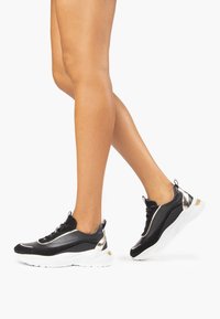 Baskets de sport noires et dorées avec une finition lisse, semelle blanche, et un design élégant comportant des accents texturés et des détails de lacets.