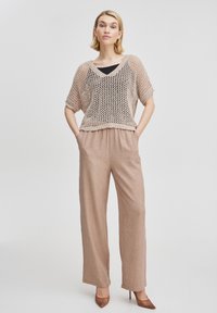 Beige stickad topp med lös passform och V-ringning, kombinerad med beiga vida byxor, avslutad med spetsiga klackskor. Slät struktur.