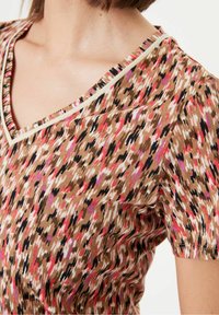Hnědý vzorovaný top s výstřihem do V, který má živé růžové, černé a krémové akcenty; měkká struktura a krátké rukávy.