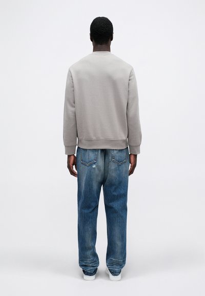Sivý bavlnený sveter s rebrovanými manžetami a spodným lemom, v kombinácii s voľne strihanými vyblednutými modrými džínsami a bielymi teniskami, pohľad zozadu.
