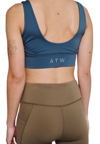 Blå atletisk crop top med brede stropper og lav ryg, med et logo mærke "ATW" ved taljen, parret med højtaljede olivengrønne leggings.