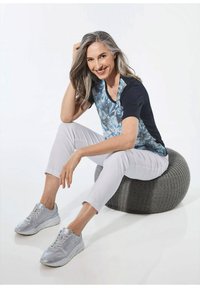 Korte mouw navy top met een blauw bloemenpatroon, lichtgrijze cropped broek en zilveren sneakers, zittend op een grijze textuurpouf.