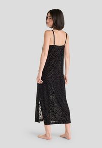 Vestido maxi de estampado de leopardo negro con tirantes finos y una abertura lateral, confeccionado en una tela ligera con una textura transparente.