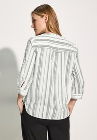 Camicia a righe bianche e nere con maniche a trequarti, dotata di un yoke sul retro e dettagli di tasche sottili, realizzata in tessuto leggero.