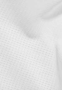 Texturerad vit tyg med ett subtilt andningsbart mönster, som visar en slät yta och lätt glans. Flexibelt och lätt material.