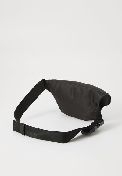 Sac de taille noir avec un extérieur en tissu doux, de forme incurvée et une sangle réglable. Équipé d'une fermeture éclair et d'un design minimaliste.