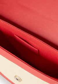 Interno di una borsa in pelle rossa con una texture liscia, dotato di un pannello intrecciato chiaro e una chiusura circolare in oro.