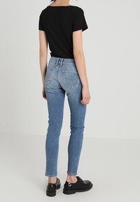 Camiseta negra ajustada de canalé combinada con jeans skinny azul claro. Tejido texturizado y diseño clásico de cinco bolsillos. Zapatos negros completan el look.