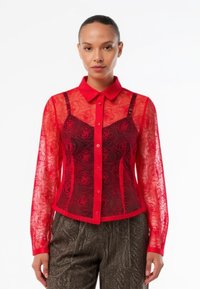 Red sheer blouse with floral lace design, button-down closure, and collar. Features a fitted bodice with straps over a dark red base.