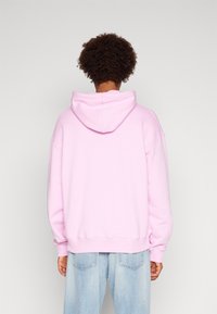 Felpa rosa in cotone con cappuccio regolabile, vestibilità oversize, polsini e orlo a coste, abbinata a jeans di denim blu chiaro. Vista posteriore.