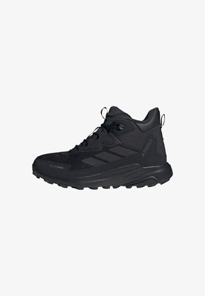 Zapatos deportivos negros con un diseño de caña alta, que presentan materiales de malla y sintéticos, una suela de goma texturizada y detalles de marca minimalistas.