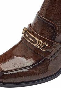 Bottine en cuir vernis marron avec un bout carré, équipée d'une bride ornée d'une chaîne en or et d'une plaque avec logo sur le côté.