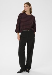 Prúžkovaný oversized sveter v bordovej a čiernej farbe v kombinácii s voľnými čiernymi nohavicami a čiernymi čižmami s kónickou špičkou. Obsahuje priliehavý pás a jemnú štruktúru.