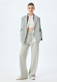 Grijze oversized blazer met dubbele knopen over een kort wit topje en lichtgrijze joggingbroek. Gladde stof met een relaxte pasvorm en een elastische tailleband.