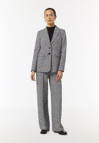 Blazer im Hahnentrittmuster und weit geschnittene Hose aus schwarzem und weißem Stoff. Merkmale sind eine taillierte Passform, zwei Knöpfe und Seitentaschen.