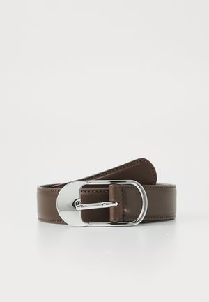 Ceinture en cuir marron foncé avec une grande boucle ovale argentée brillante, reposant enroulée sur une surface blanche.