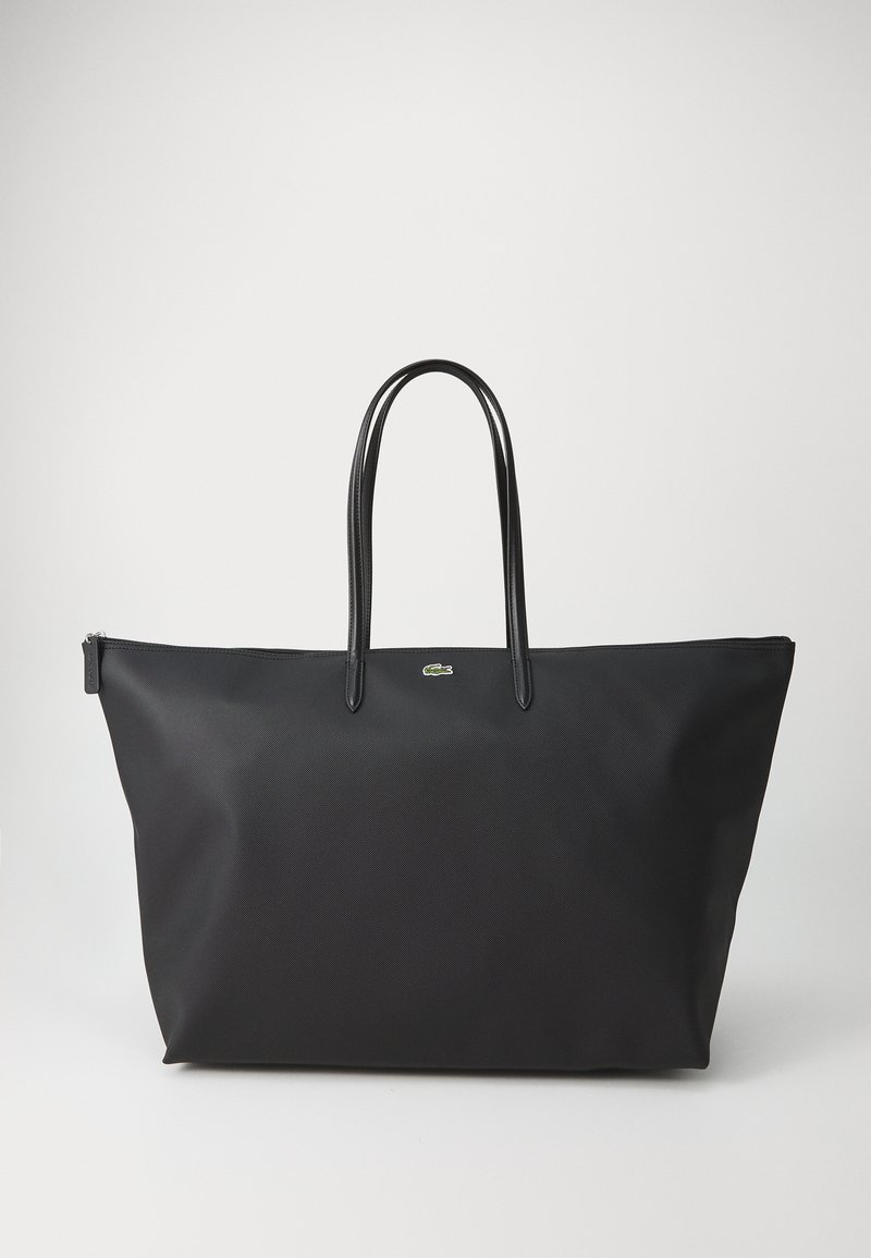 Sac fourre-tout noir avec un corps en nylon texturé, de fines poignées noires, et un petit accent de logo vert. Fermeture zippée en haut.
