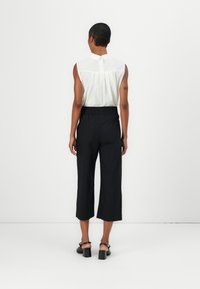 Blusa bianca senza maniche con colletto e schiena plissettata, abbinata a pantaloni neri alla caviglia. L'outfit presenta una vestibilità comoda e una vita elasticizzata.