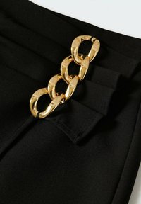 Sort stof med plisseringer og en fremtrædende guldkæde, som accentuerer siden. Kæden har store, sammenkoblede led.