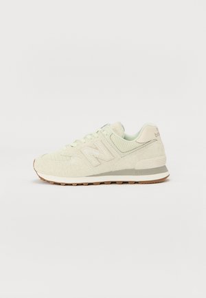 Light-colored sneaker with a textured upper, featuring a lace-up design and a cushioned sole. Accented with a subtle “N” logo on the side.